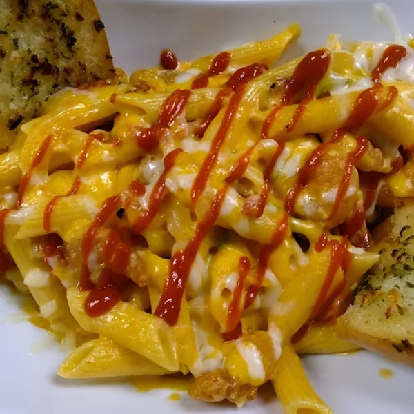 Penne pasta with melted cheese, drizzled with red sauce, and two pieces of garlic bread.