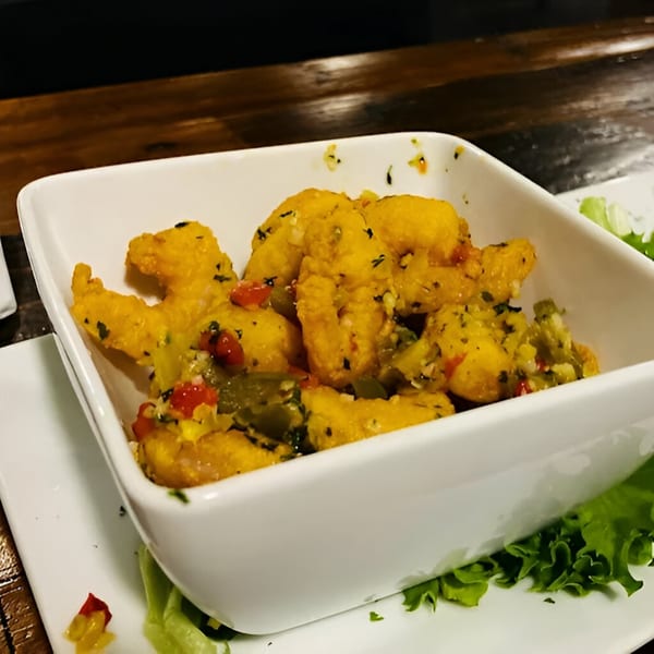 A white rectangular bowl filled with golden-fried shrimp and colorful diced vegetables, garnished with lettuce.