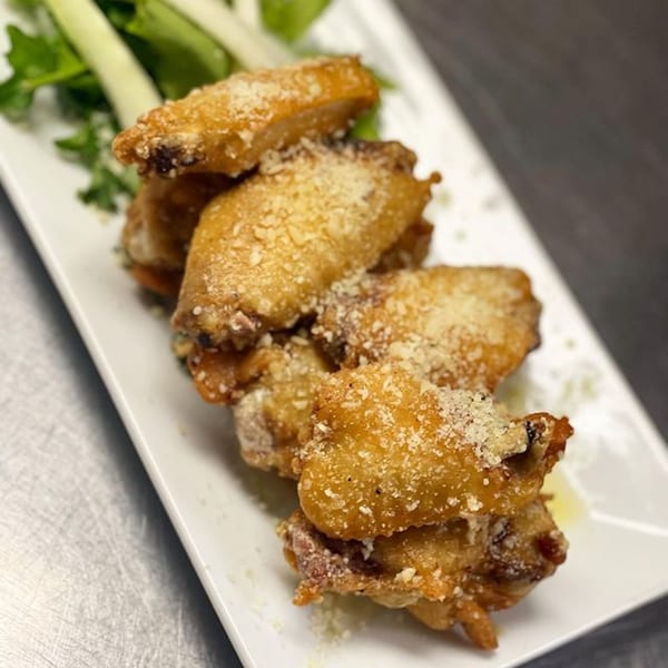 Crispy fried chicken wings, dusted with parmesan cheese, served on a white plate with celery.