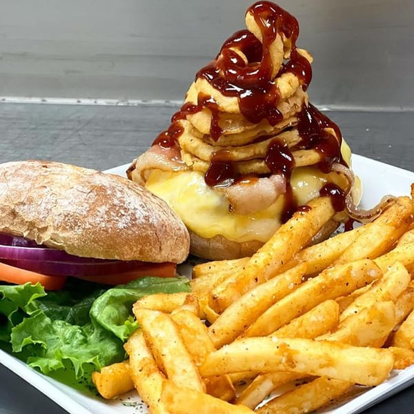 A burger with a towering stack of onion rings and BBQ sauce, served with fries and salad.