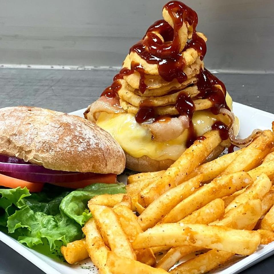 A burger with a towering stack of onion rings and BBQ sauce, served with fries and salad.